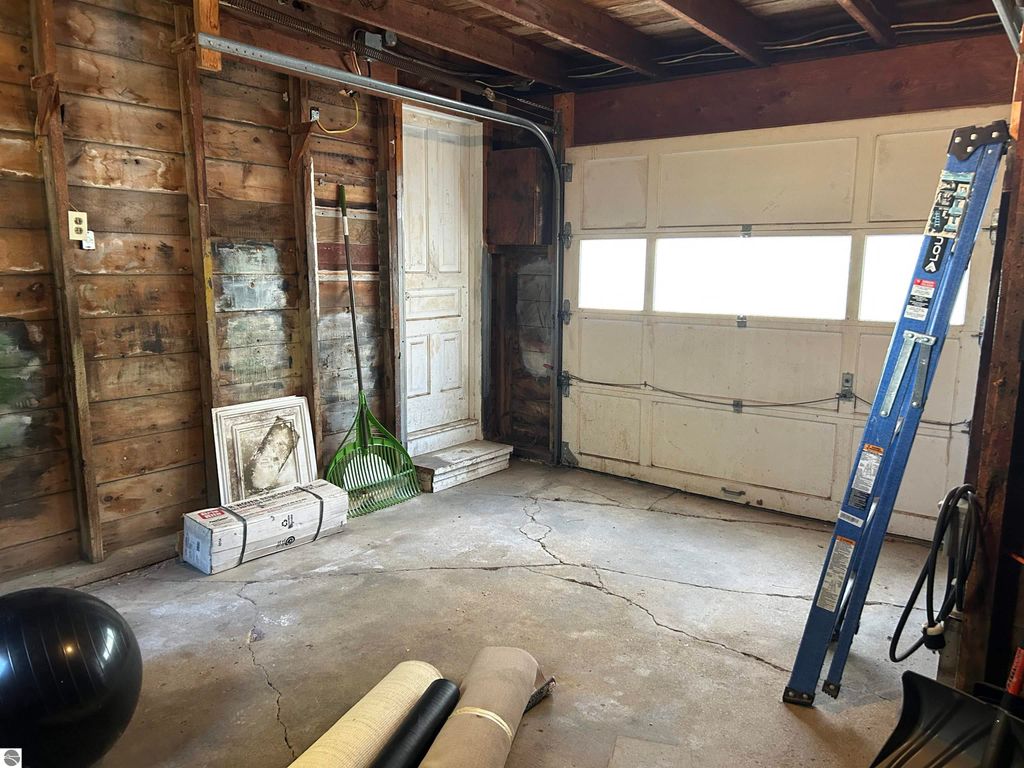 Interior view of a garage with wooden walls, a white door, a ladder, and various storage items including a black exercise ball, rolled mats, and a rake, highlighting the property's potential for a workshop or craft space at 11138 W 2nd Street, Fowler, MI.