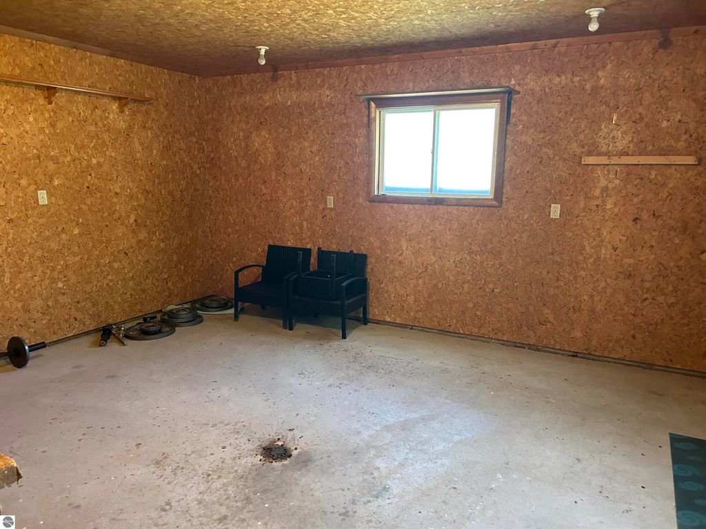 Interior view of a detached woodshop or craft room with cork walls, a window, two black chairs, and exercise weights on the floor, showcasing potential for storage or creative use in the property at 11138 W 2nd Street, Fowler, MI.