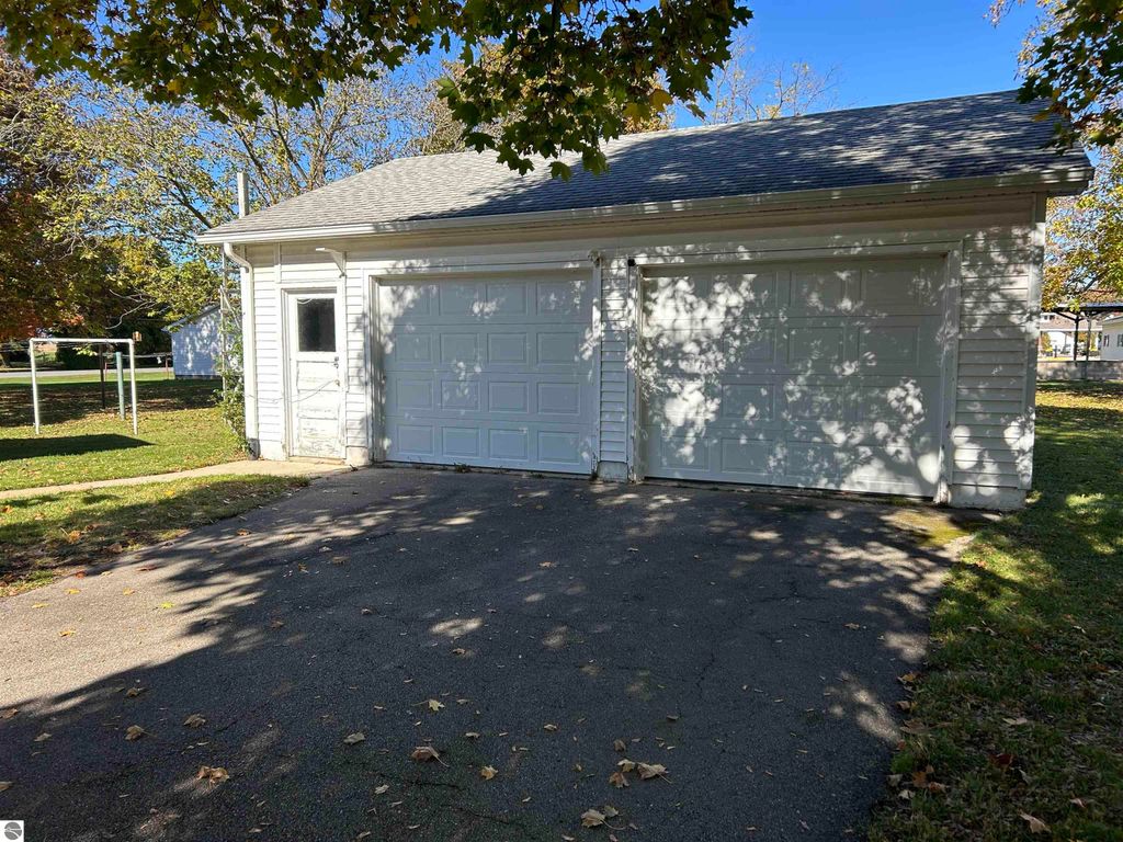 Detached two-car garage with white siding and two garage doors, surrounded by a large yard featuring mature trees, located at 11138 W 2nd Street, Fowler, MI.