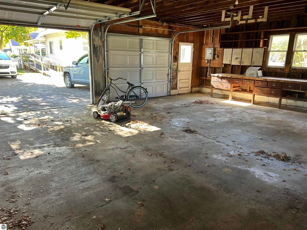 Garage interior with a bicycle and lawn mower, featuring an open door, concrete floor, and wooden workbench, showcasing storage potential for the 4-bedroom home at 11138 W 2nd Street, Fowler, MI.