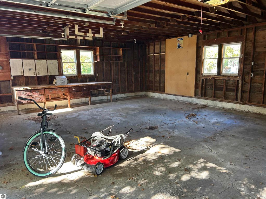 Garage interior featuring a bicycle and lawn mower, with wooden shelves and windows, highlighting potential for storage or workspace in the 4-bedroom home at 11138 W 2nd Street, Fowler, MI.