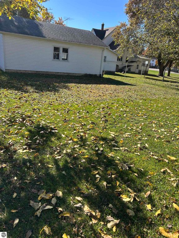 Backyard view of 11138 W 2nd Street, Fowler, MI, featuring a spacious lawn with fallen leaves, adjacent houses, and a side view of the home.