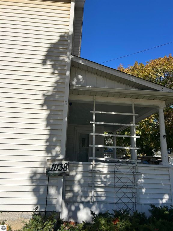 Front view of 11138 W 2nd Street, Fowler, MI, featuring a white house with a porch, house number visible, and clear blue sky.