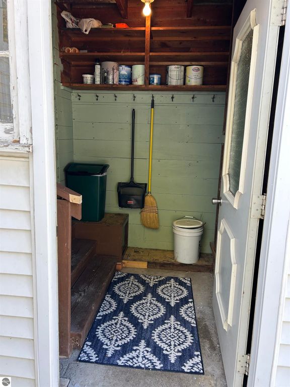 Entryway with stairs, broom, trash can, and storage shelves, featuring a decorative rug, in a home located at 11138 W 2nd Street, Fowler, MI.