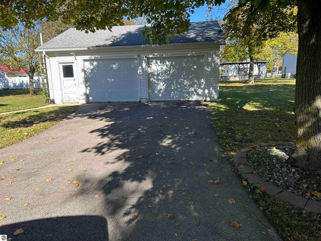 Detached two-car garage with a paved driveway, surrounded by mature trees and a grassy yard, located at 11138 W 2nd Street, Fowler, MI.