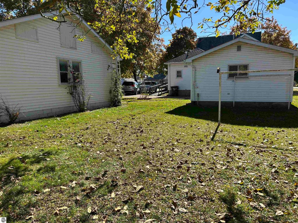 Exterior view of a residential property at 11138 W 2nd Street, Fowler, MI, featuring two white houses, a grassy yard with fallen leaves, and a clothesline, highlighting the spacious outdoor area suitable for family activities.