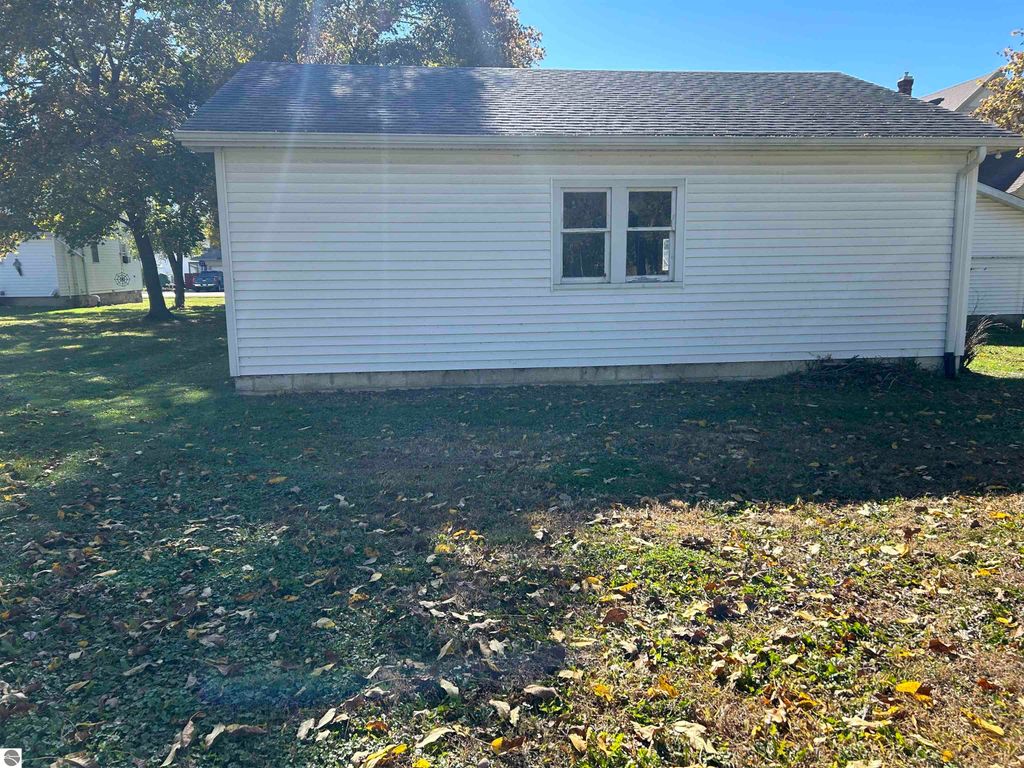 Exterior view of a single-story home at 11138 W 2nd Street, Fowler, MI, featuring a white siding facade, two windows, and a grassy yard with fallen leaves.