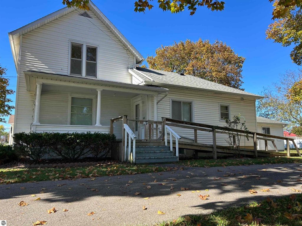 Exterior view of a two-story home at 11138 W 2nd Street, Fowler, MI, featuring a front porch, wooden ramp, and surrounding autumn foliage.