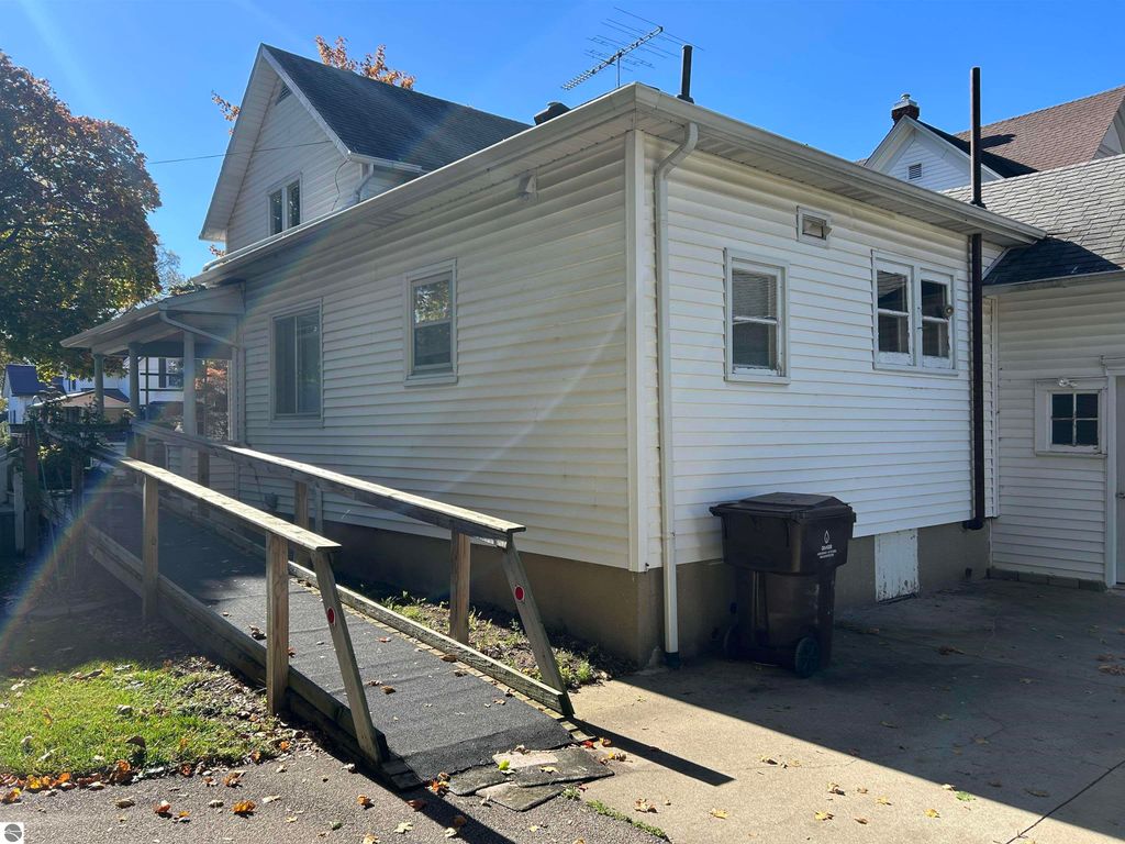 Side view of a 4-bedroom home at 11138 W 2nd Street, Fowler, MI, featuring a wheelchair-accessible ramp, large windows, and a detached garage, set in a neighborhood with mature trees.