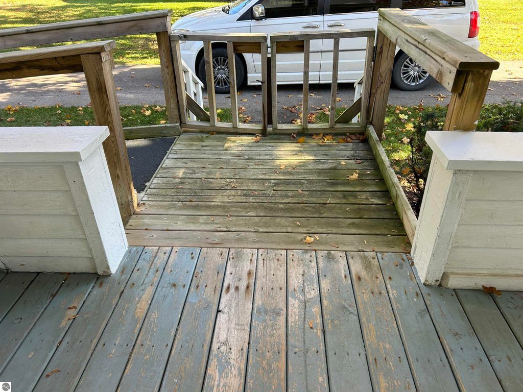 Wooden porch entrance with steps leading down, surrounded by white railings and a view of a parked vehicle, showcasing the outdoor space of the property at 11138 W 2nd Street, Fowler, MI.