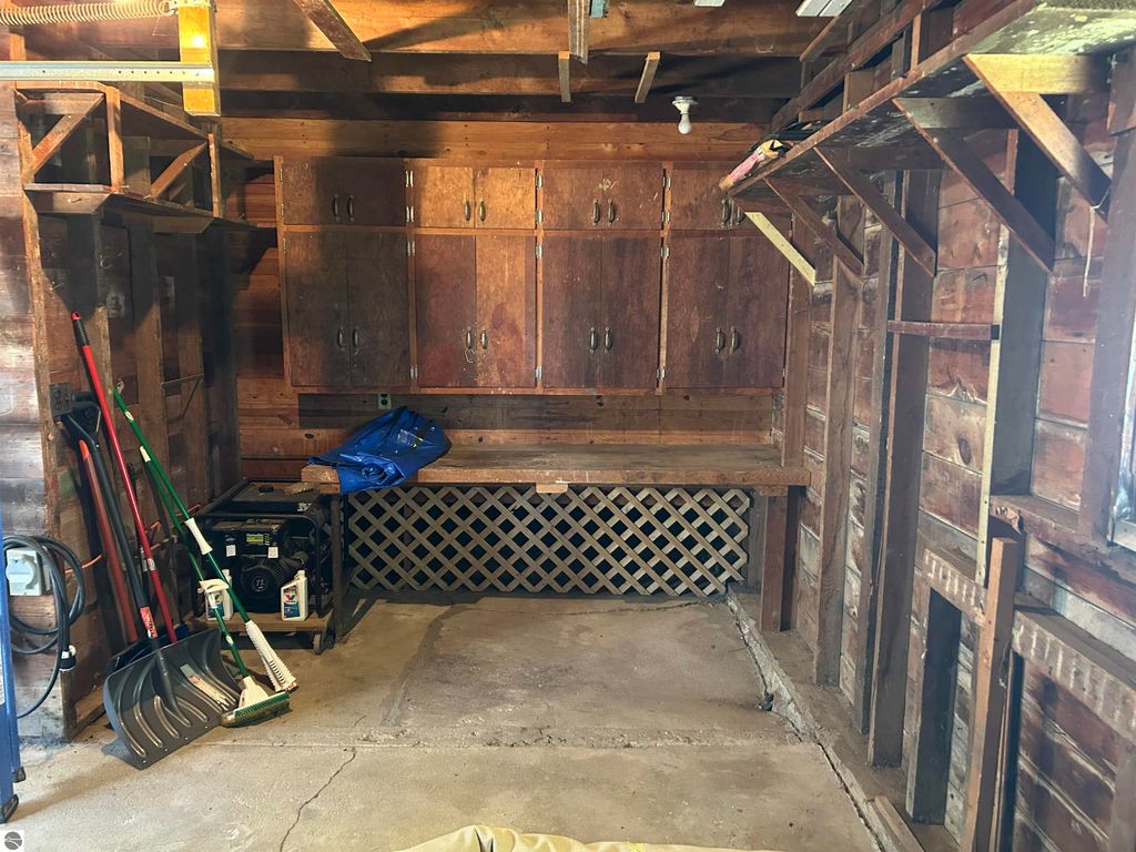 Interior view of a garage featuring wooden storage cabinets, a workbench, gardening tools, and a generator, highlighting potential for a craft or workshop space at 11138 W 2nd Street, Fowler, MI.