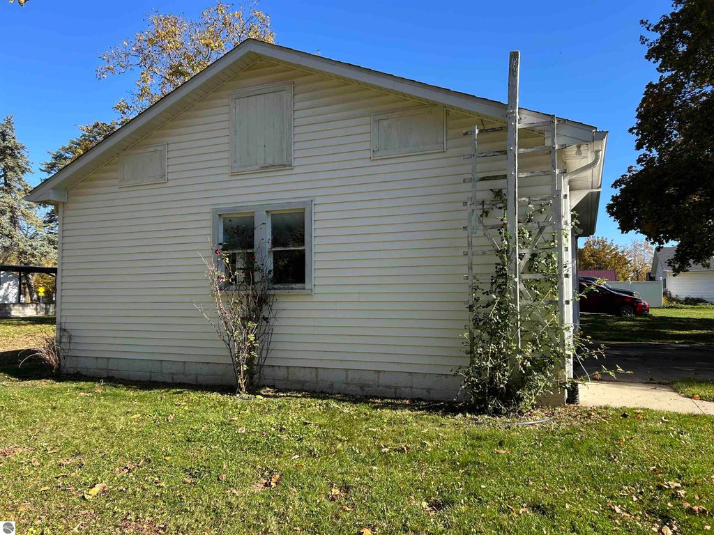 Exterior view of a white house located at 11138 W 2nd Street, Fowler, MI, featuring a sloped roof, window with greenery, and a yard with grass, suitable for potential buyers.