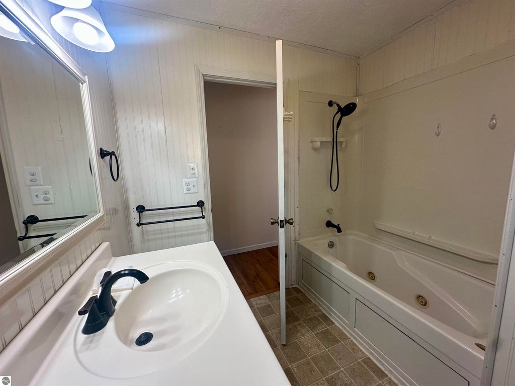 Bathroom interior featuring a sink with a modern faucet, a large mirror, and a bathtub with a showerhead, showcasing a clean and inviting design relevant to the real estate listing at 8398 W Whispering Pines, Lake City, MI.