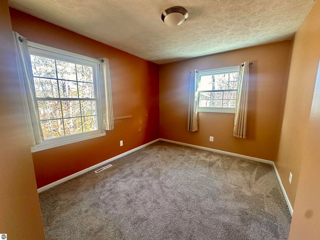 Cozy bedroom with brown walls, large windows, and soft carpet, showcasing a serene atmosphere in a Lake City home for sale.