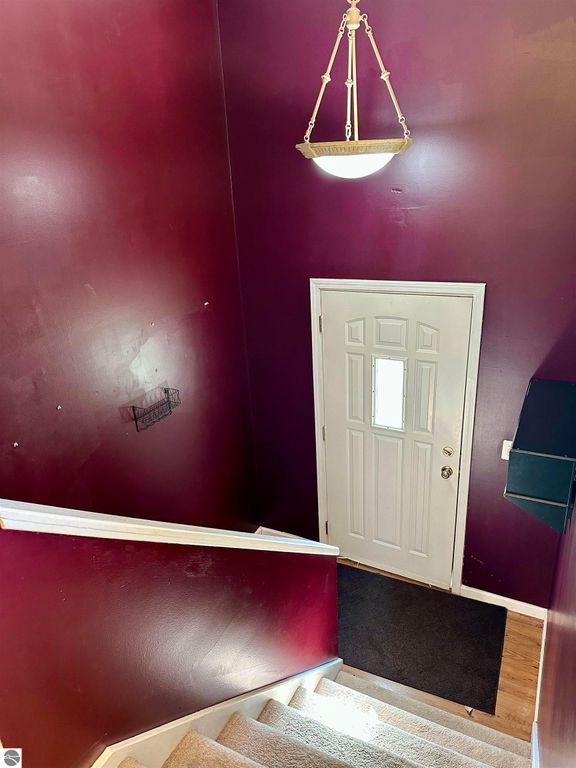 Entryway of bi-level home at 8398 W Whispering Pines, featuring a burgundy wall, white door, and staircase leading to the upper level.
