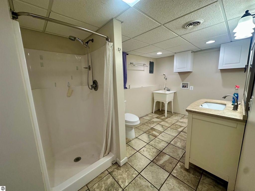 Updated bathroom featuring a shower, toilet, and sink with a countertop, showcasing tiled flooring and modern fixtures in a well-lit space.