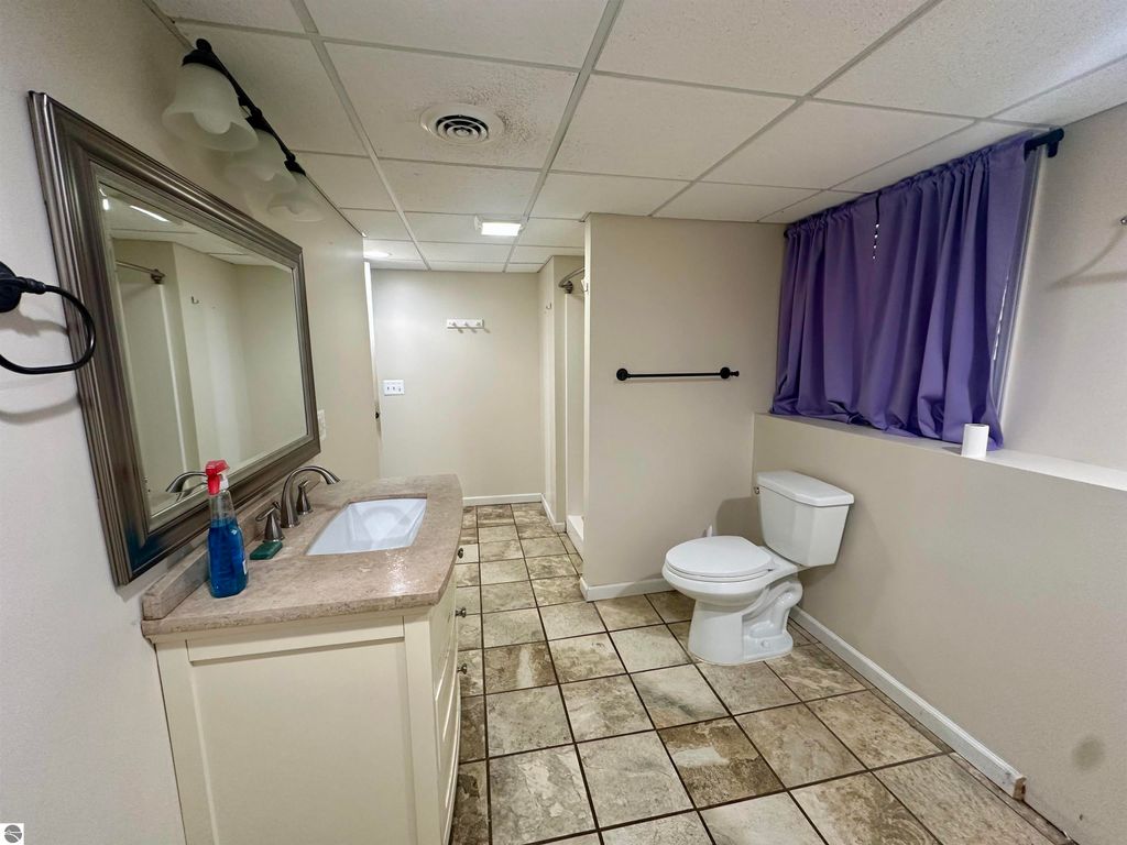 Bathroom interior featuring a sink with modern fixtures, a large mirror, tiled flooring, and a toilet, complemented by a window with purple curtains, showcasing the updated amenities of the Lake City home listing.