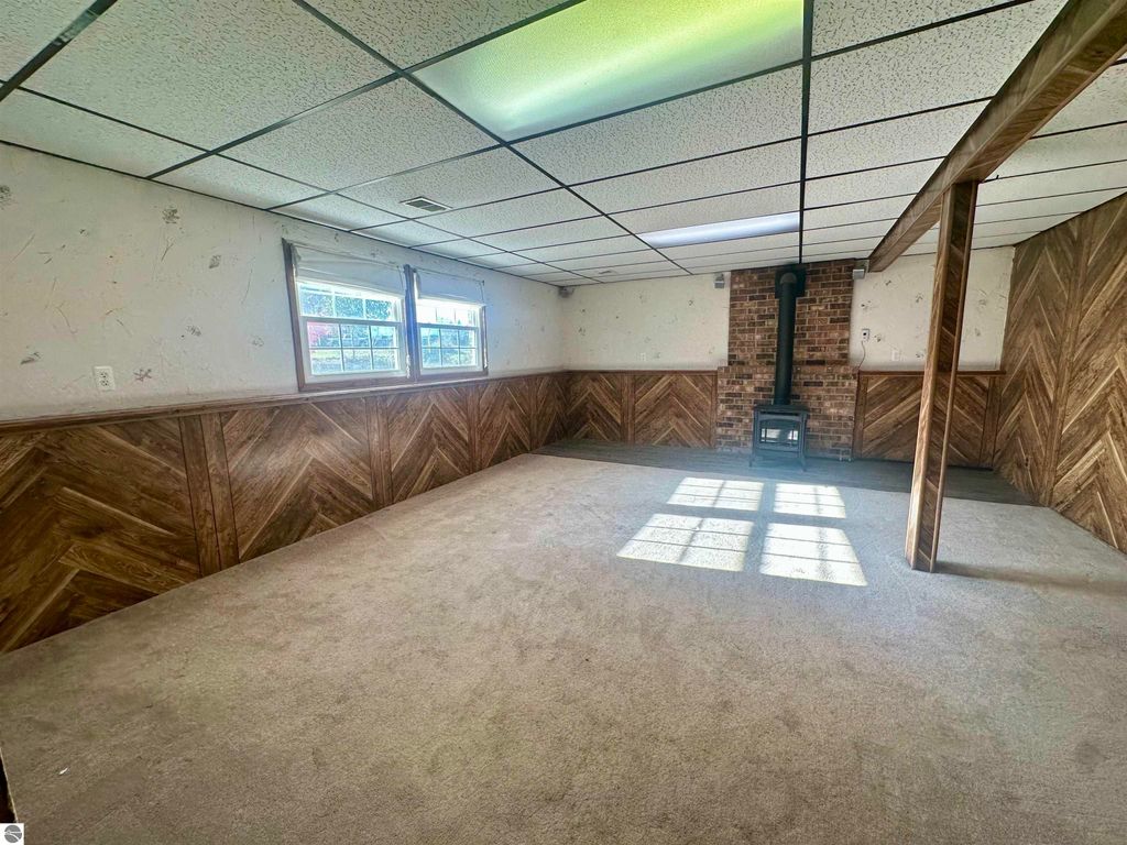 Bi-level interior space with carpeted flooring, large windows allowing natural light, and a wood-burning stove against a brick wall, showcasing a cozy atmosphere in a Lake City home.
