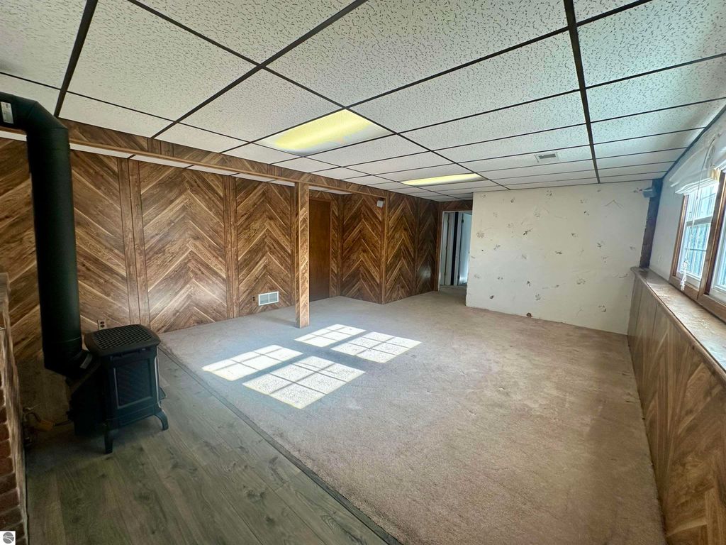 Bi-level interior with herringbone wood paneling, carpeted floor, and a corner stove, showcasing a spacious layout in Lake City, MI home listing.