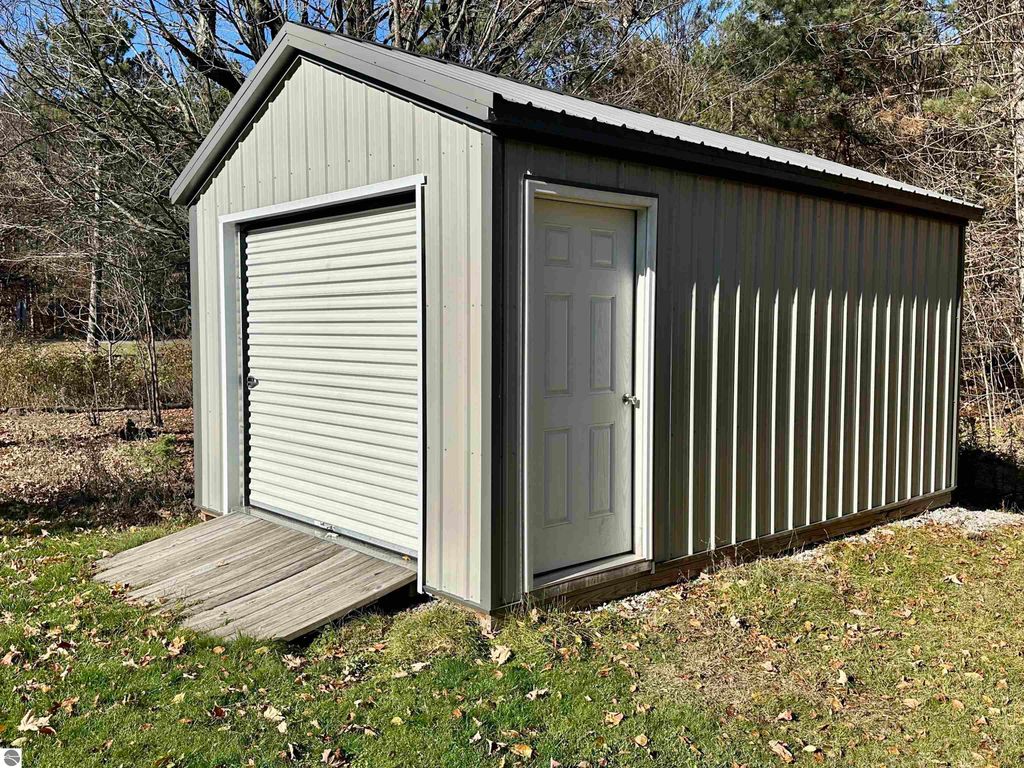 Garden shed with roll-up door and side entry, surrounded by wooded area, located on nearly three-quarters of an acre property in Lake City, MI.