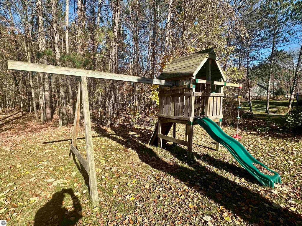 Playground set with a slide and swings in a wooded backyard, showcasing a private outdoor space ideal for family activities near 8398 W Whispering Pines, Lake City, MI.