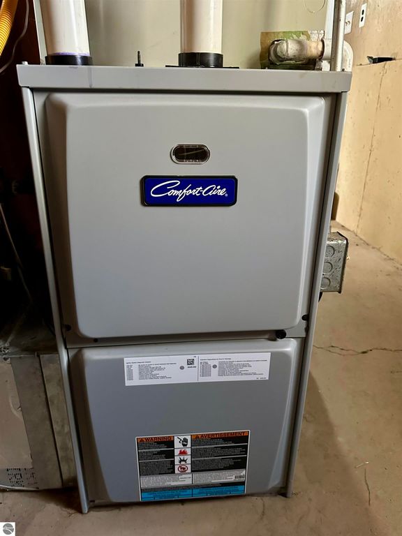 Comfort Aire furnace with visible warning label, located in a basement setting, highlighting updated heating system for residential property at 8398 W Whispering Pines, Lake City, MI.