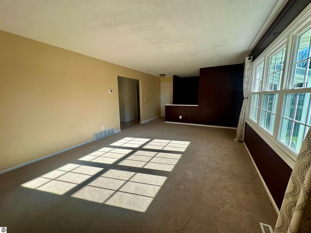 Spacious living room in bi-level home at 8398 W Whispering Pines, featuring natural light from large windows, neutral wall colors, and carpet flooring.