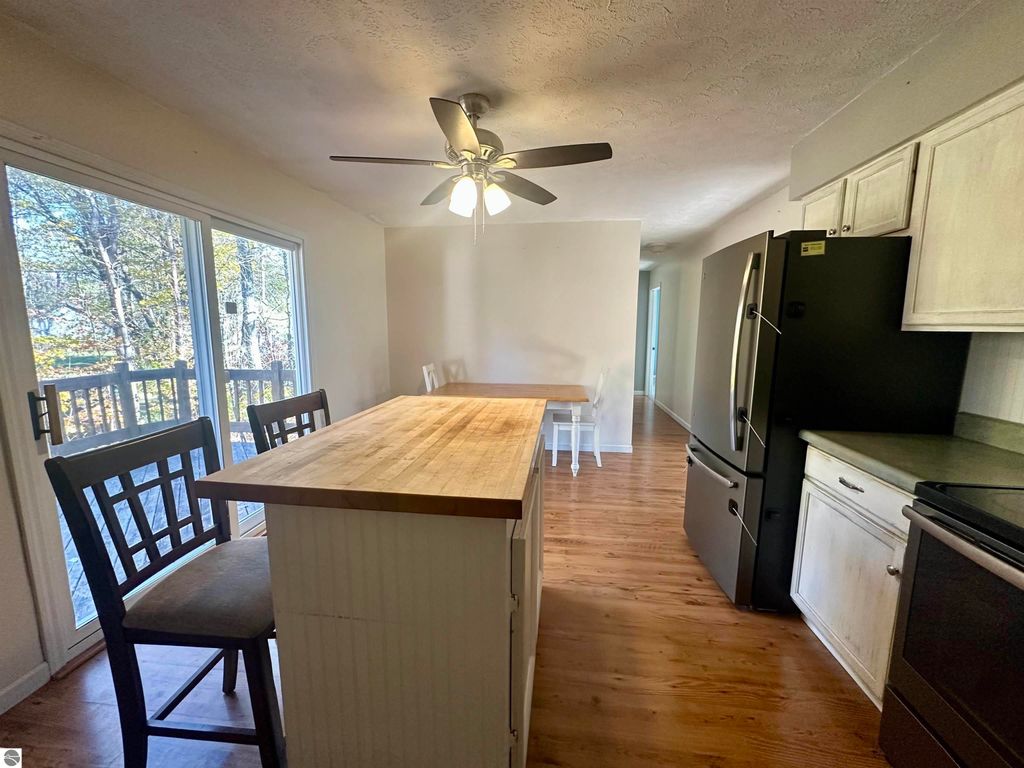 Bright, inviting kitchen featuring a wooden island with seating, black appliances, and large windows overlooking a wooded backyard, showcasing a modern, open layout ideal for entertaining in the Lake City, MI home at 8398 W Whispering Pines.