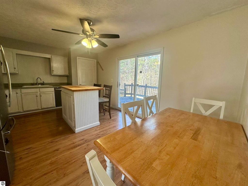 Bi-level kitchen interior featuring a wooden dining table, white chairs, modern appliances, and large sliding glass doors leading to a raised deck overlooking a wooded backyard, showcasing a warm and inviting atmosphere.