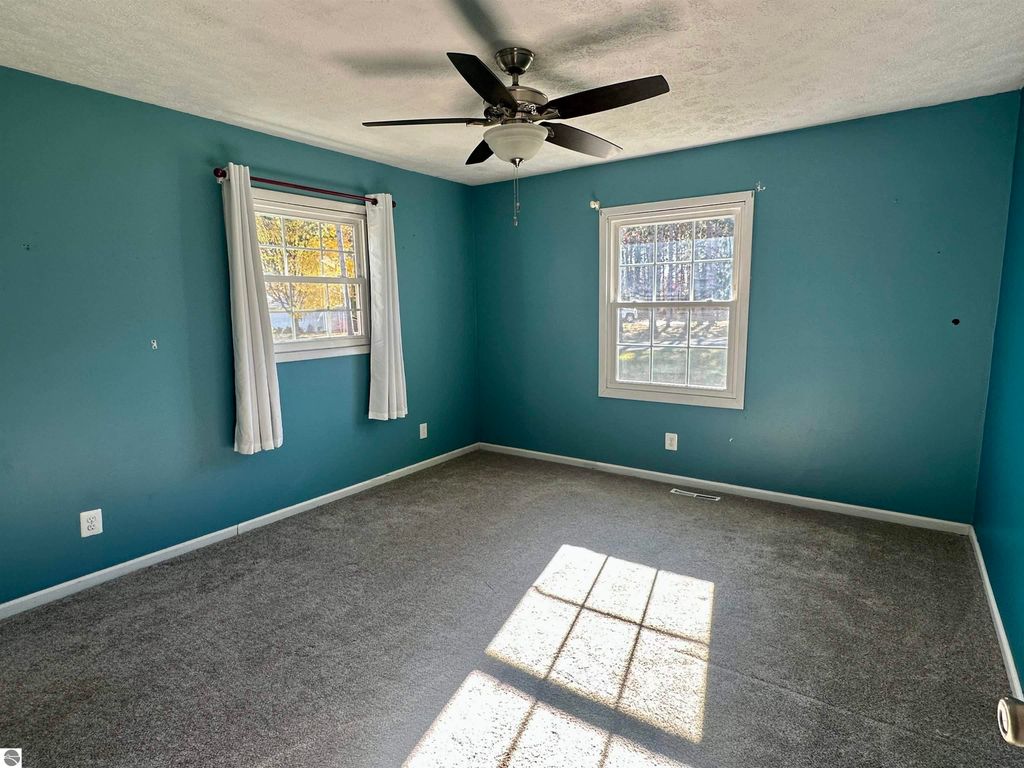 Spacious bi-level bedroom with teal walls, large window, ceiling fan, and natural light illuminating the carpeted floor, showcasing the inviting interior of the home at 8398 W Whispering Pines, Lake City, MI.
