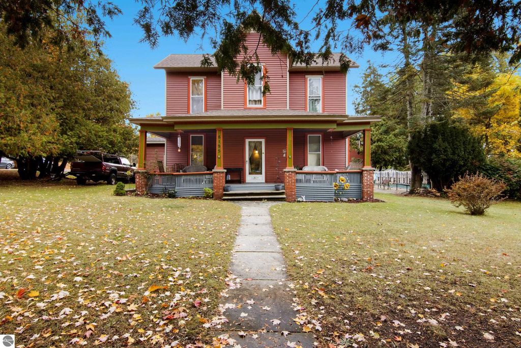 Victorian-style home at 8195 Fifth Street, Onekama, MI, featuring original wood trim, inviting porch, and landscaped yard with autumn leaves.