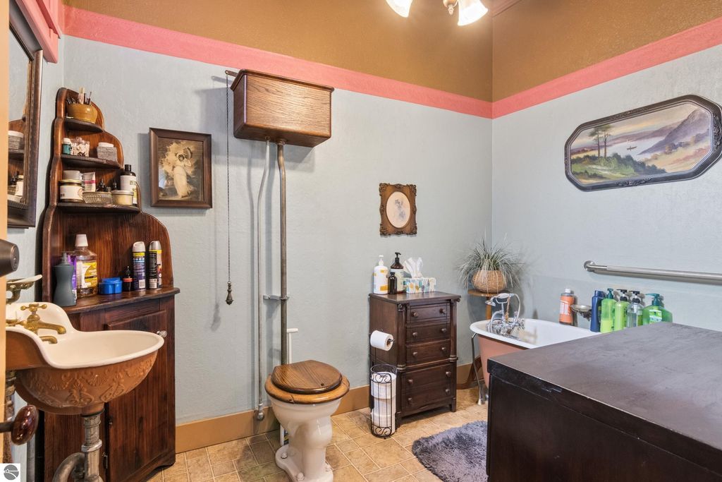 Victorian-style bathroom featuring a vintage sink, wooden toilet, clawfoot tub, and original decor elements, reflecting the charm of the 1880 home in Onekama, MI.