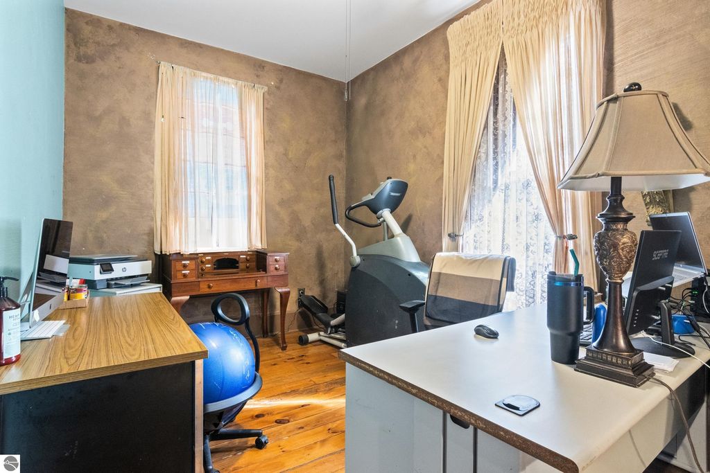 Home office with vintage decor, featuring wooden desk, exercise equipment, computer setup, and natural light from window with sheer curtains.