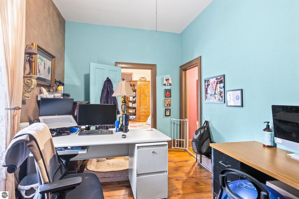Home office setup in a Victorian house, featuring a white desk with dual monitors, wooden flooring, and turquoise walls, showcasing a blend of modern and classic decor elements.