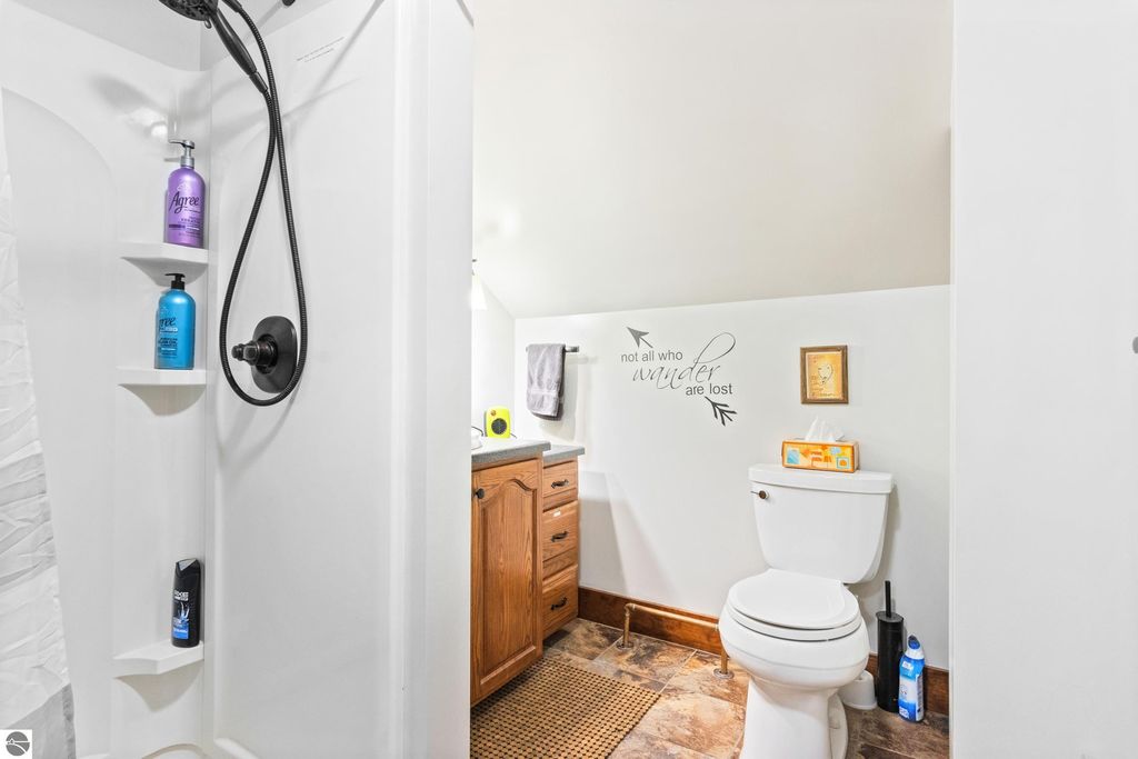 Bathroom with shower featuring toiletries, wooden cabinetry, and decorative wall art reading "not all who wander are lost."