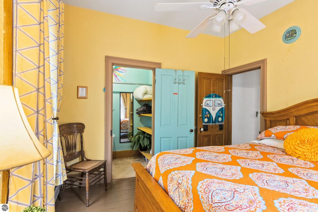 Victorian-style bedroom featuring an orange patterned bedspread, wooden furniture, and a cozy atmosphere, with an adjoining room visible through a turquoise door, highlighting the home's charm and character in Onekama, MI.
