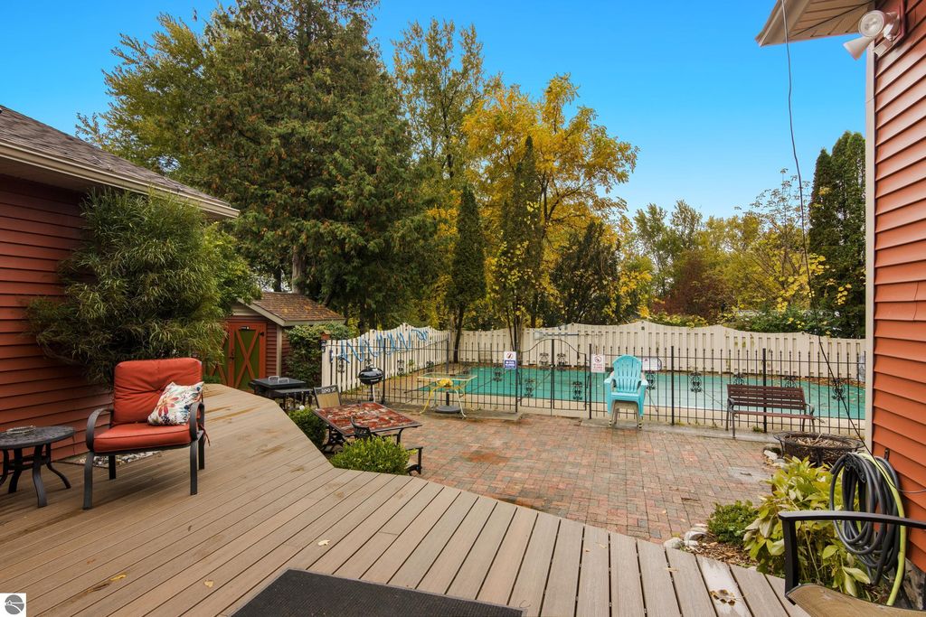 Backyard view of Victorian home in Onekama, featuring in-ground pool, patio seating, and lush greenery, highlighting outdoor amenities for potential bed and breakfast use.