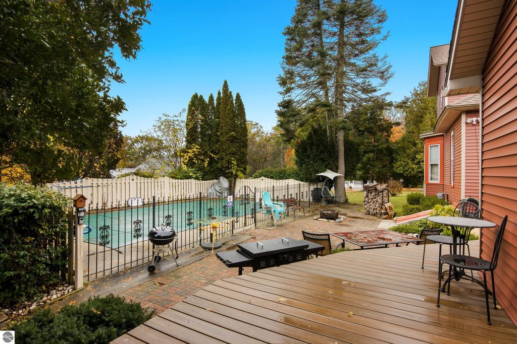 Backyard view of Victorian home in Onekama, featuring in-ground pool, patio area with seating, and surrounding greenery, highlighting resort-style amenities and outdoor living space.