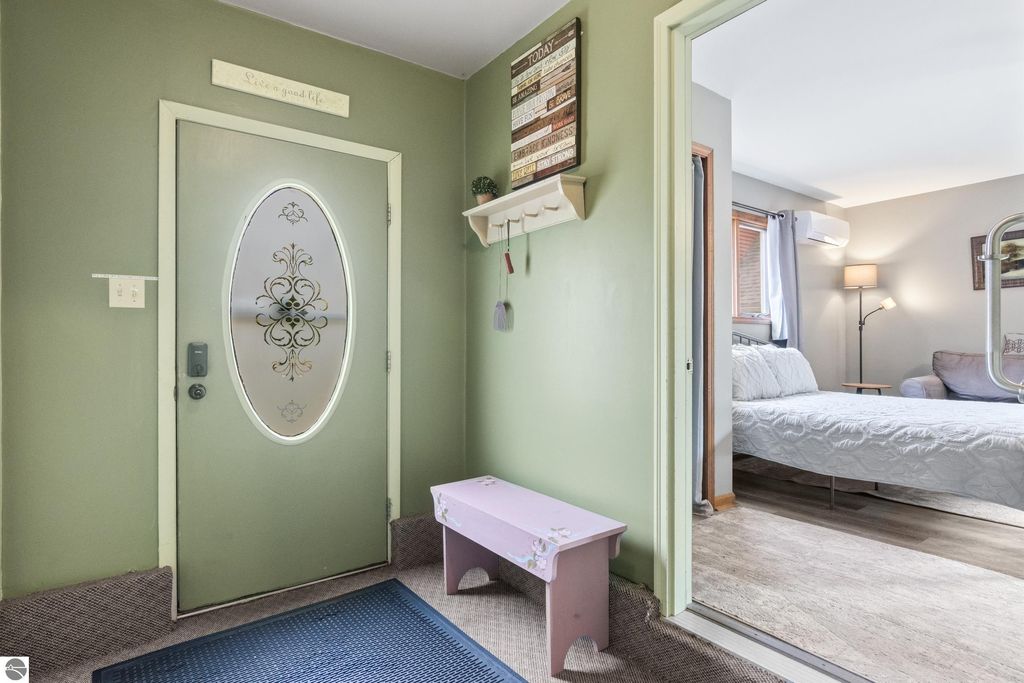 Victorian entryway with green walls, decorative door, and pink bench, leading to a cozy bedroom space, reflecting the charm of the 1880 home in Onekama, MI.