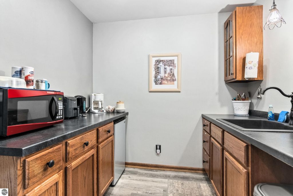 Kitchen area with black countertops, wooden cabinets, red microwave, coffee maker, and decorative wall art, showcasing a cozy space in the Victorian home for sale in Onekama, MI.