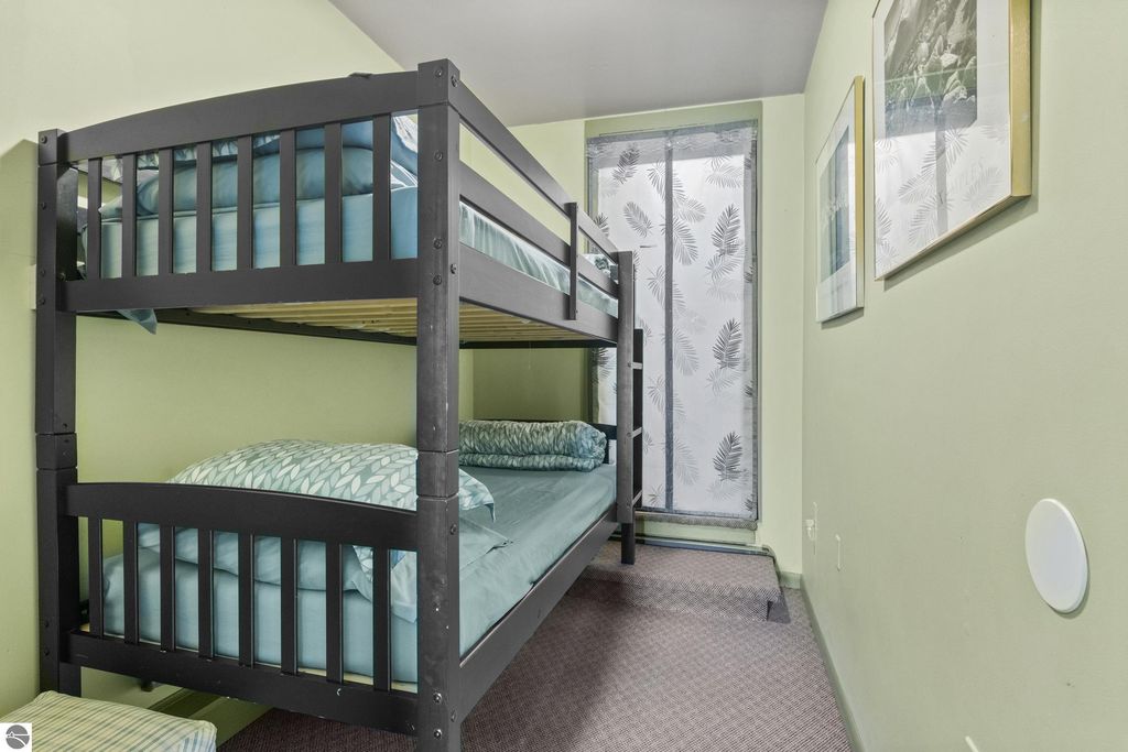 Bunk beds with teal bedding in a cozy room featuring light green walls and a window with sheer leaf-patterned curtains, suitable for a bed and breakfast setting.