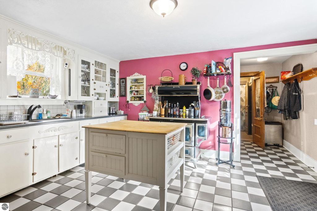 Victorian-style kitchen featuring white cabinetry, a central island, black and white checkered floor, and a vibrant pink accent wall, showcasing a blend of classic charm and modern amenities.