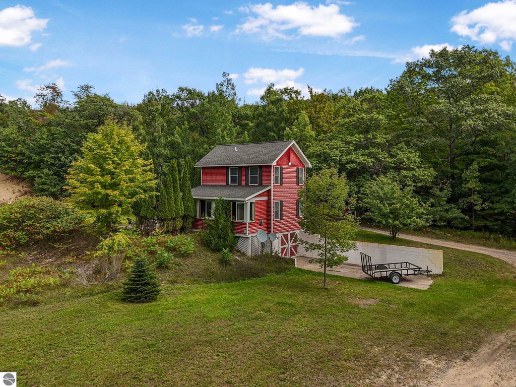 Elevated red farmhouse at 5361 N Manitou Trail, surrounded by trees and greenery, featuring a shared driveway and outdoor space on 3 acres near Leland, MI.