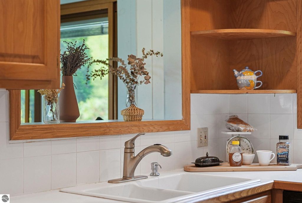 Kitchen sink with modern faucet, wooden cabinetry, decorative vases with dried flowers, and countertop items including honey, a coffee mug, and a teapot, showcasing a cozy farmhouse atmosphere in the property listing at 5361 N Manitou Trail, Leland, MI.