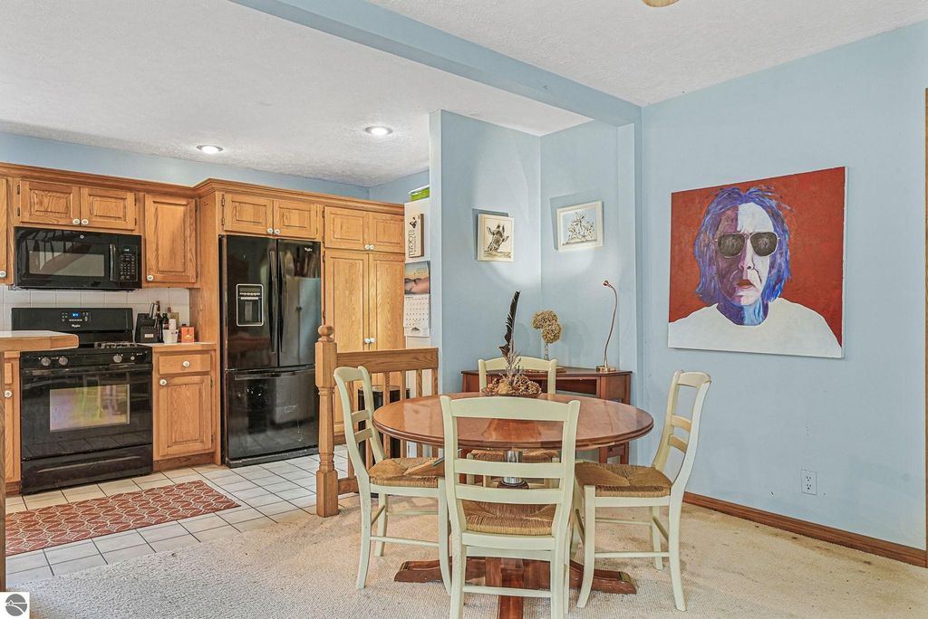 Kitchen area featuring wooden cabinets, black appliances, and a round dining table with chairs, complemented by a colorful wall art piece, in a cozy farmhouse setting near Leland, MI.