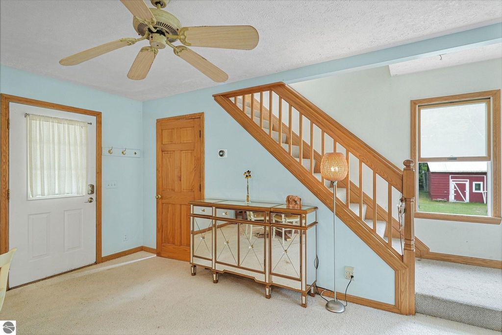 Interior view of a cozy entryway in a farmhouse, featuring wooden staircase, decorative lamp, and a mirrored console table, with a window revealing a glimpse of a red barn outside.