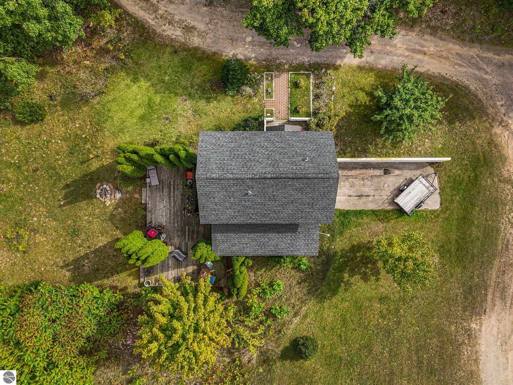 Aerial view of a farmhouse surrounded by greenery on 3 acres, featuring a wooden deck, outdoor seating, and a shared driveway in Leland, MI.