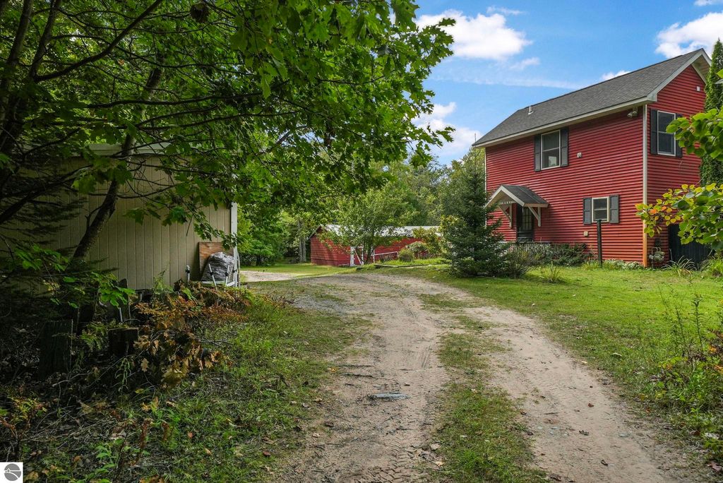 Red farmhouse at 5361 N Manitou Trail, surrounded by trees and greenery, with a dirt driveway leading to the home and additional outbuilding visible in the background.