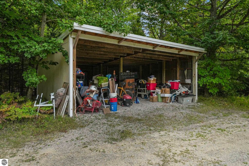 Storage shed filled with various items, including tools, boxes, and containers, surrounded by greenery near 5361 N Manitou Trail, Leland, MI.