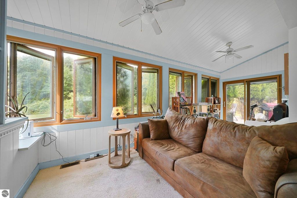 Cozy living area with large windows showcasing natural light, brown couch, and wooden furniture, highlighting the inviting interior of the farmhouse at 5361 N Manitou Trail, Leland, MI.